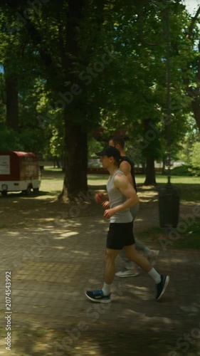 Two men are running through a lush green park on a bright sunny day. They share an active and healthy outdoor workout experience.