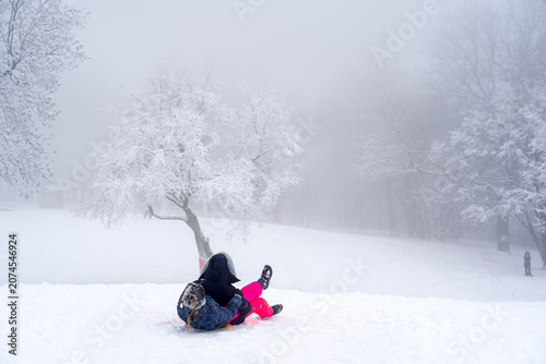 Konstfotografi Two children tumbling and laughing while sledding down a snowy hill into thick w