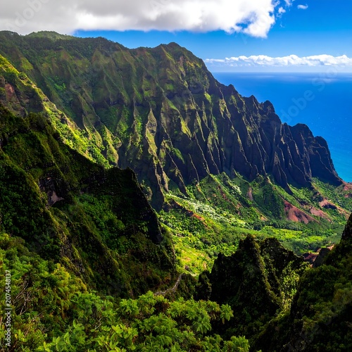 Dramatic Green Mountain Cliffs Overlooking Blue Ocean Coastline Under Cloudy Sky