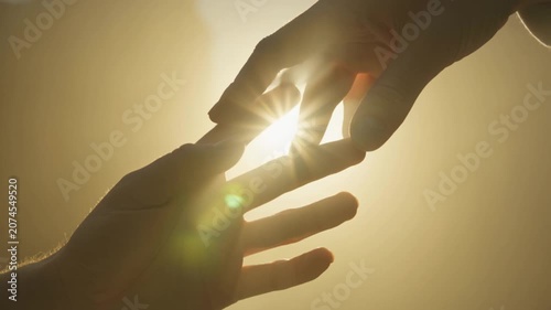 Backlit human hands reaching out to connect in glowing golden sunlight, symbolizing hope and spiritual guidance.