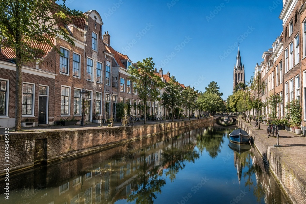 Obraz premium Serene canal in Delft with red brick houses and calm water reflection.