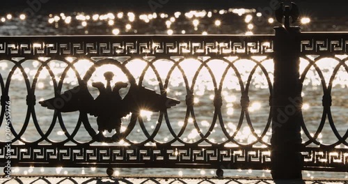 picturesque metal railings with a double-headed eagle and the crown of the Russian Empire on embankment in St. Petersburg, Russia, walking people, sunny autumn day, incredible sun glare Russia
