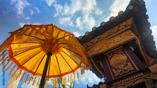 Fotografie Traditional Balinese yellow ceremonial umbrella and temple shrine carving under