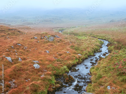 Bild auf Leinwand Winding stream flows through autumnal moorland with scattered rocks