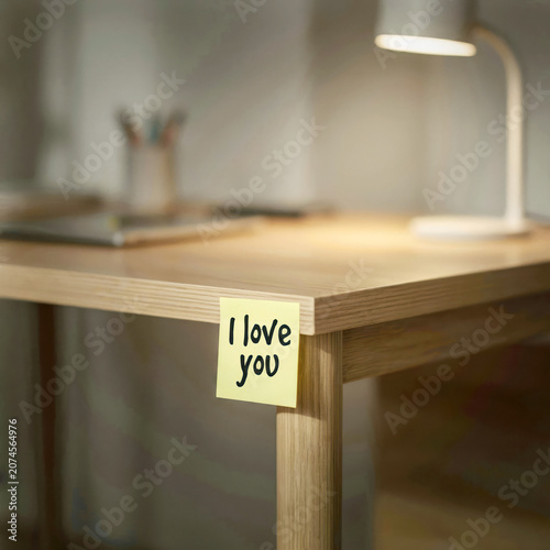 I love you written on a post-it note stuck to a wooden desk