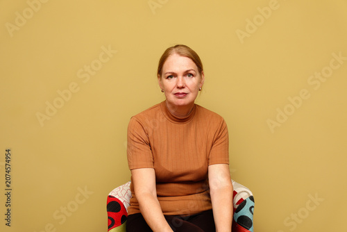 Portrait of mature middle aged woman looking at camera against olive background. elegant lady sitting in colorful armchair, retirement aging concept or mental health template with copy space
