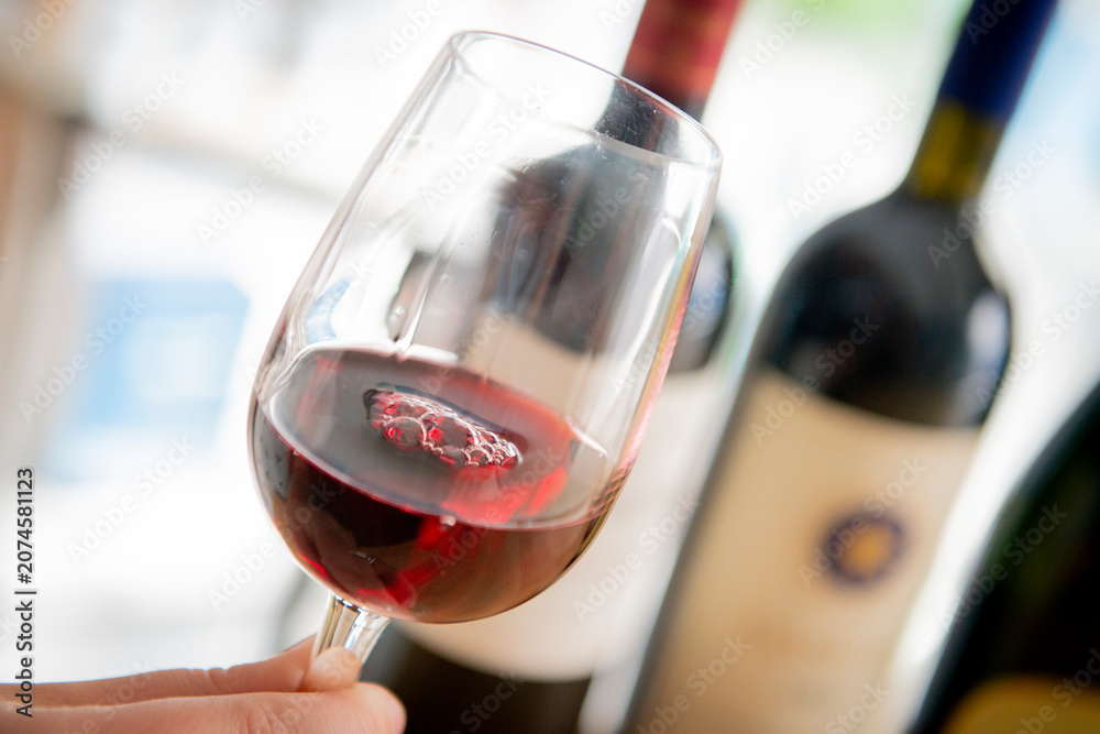 Fototapeta premium Savoring Rich Red Wine in a Cozy Setting With Elegant Bottles in View