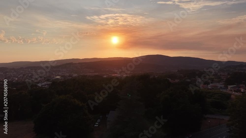 Sunset light shining over a tree silhouette with a mountain landscape and urban area