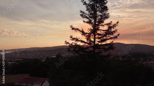 Sunset light shining over a tree silhouette with a mountain landscape and urban area