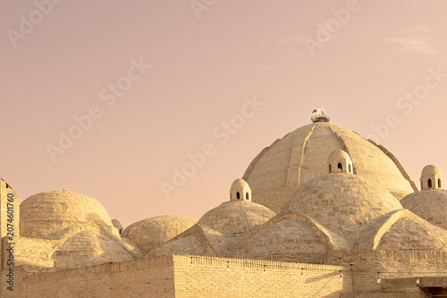 Brick domes of Toqi Zargaron covered bazaar in Bukhara with a stork nest on top against a warm sunset sky. Ideal for travel publications, cultural heritage projects, and Central Asian tourism.