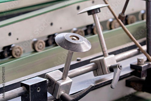 Slika na platnu Detailed view of circular guide discs mounted on a steel rail with manual adjustment levers on a manufacturing machine line