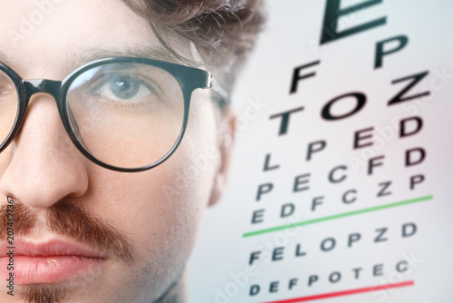 Foto Man in glasses and eye chart on white background, selective focus
