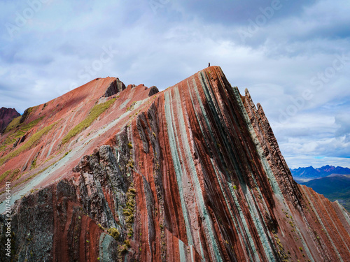 Slika na platnu Stunning Rainbow Mountain in Peru with a hiker standing on the peak under a clou