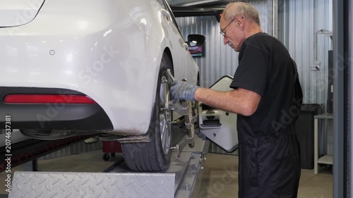 An auto mechanic installs a wheel adapter on the wheel to perform wheel alignment, balancing the wheels of the car at a service station.