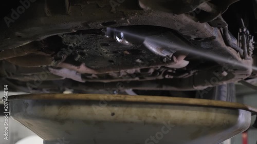 Close-up of the washing of the bottom and wheels after repair and oil change with a jet of water at a service station. The mechanic is washing the bottom of the car with a special solution.
