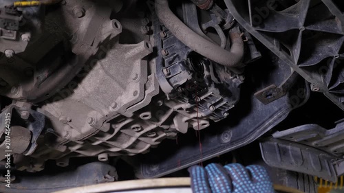 A detailed view of the underside of the vehicle after an oil change, with a stream of water at the service station. The mechanic is cleaning the underside of the car using a specialized tool.