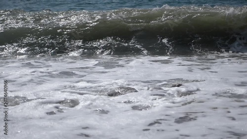 A view of large waves moving slowly. Muddy waves rise and crash against the rocky shore, forming foam. The sea during a storm.