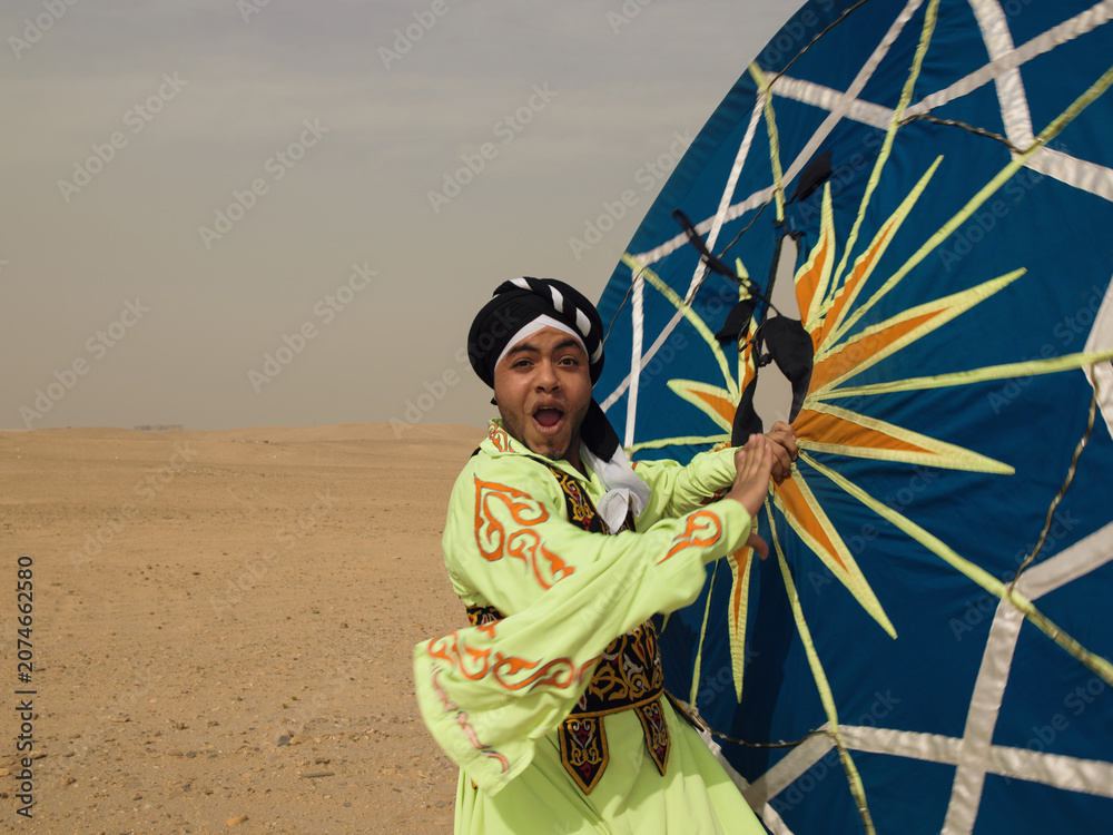 Fototapeta premium Energetic Egyptian tanoura folk dancer in vivid green costume spinning a large patterned skirt prop in the open desert ideal for cultural festival and