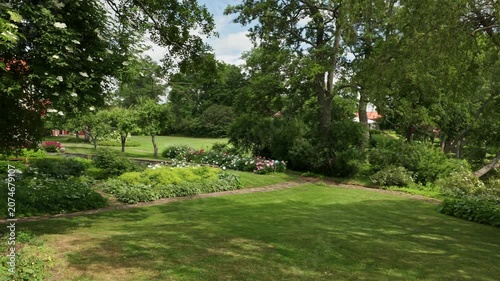 Beautiful view of landscaped garden with willow trees and flowering shrubs beside lakeshore. Sweden.