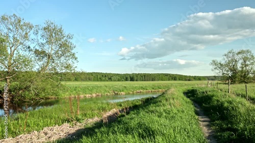 Beautiful view of grassy riverside path beside winding river against cloud-filled sky. Sweden.