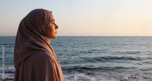 A contemplative muslim woman in hijab looking towards the ocean horizon
