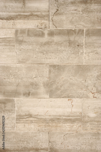 Neutral beige stone tile wall with natural surface variations and clean geometric pattern. Architectural texture background suitable for interior and exterior design concepts.