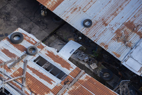 Mechanical workshop roofs, with materials scattered even on top. Two roofs with wood and tires on top, separated by a gap that reveals a mechanical workshop
