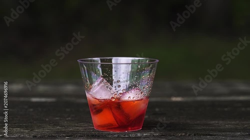 Refreshing spritz cocktail being prepared on a rustic wooden table. Bartender adds soda and garnishes the red drink with a fresh orange slice in slow motion
