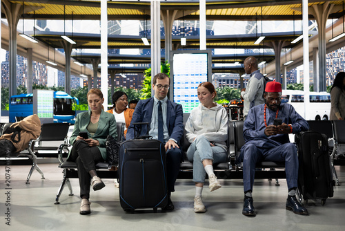 Картината върху платно Young couple waiting in crowded bus terminal before long-haul interstate journey, man and woman with luggage and carry-on bags check departure board screen