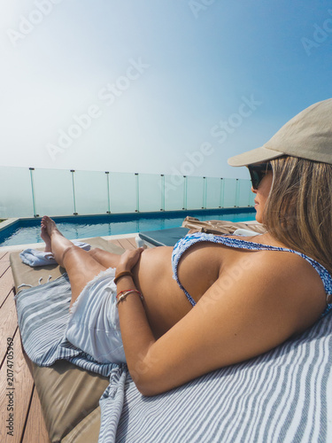 Картината върху платно Woman sunbathing on a cushioned lounger beside an infinity pool with a clear blu