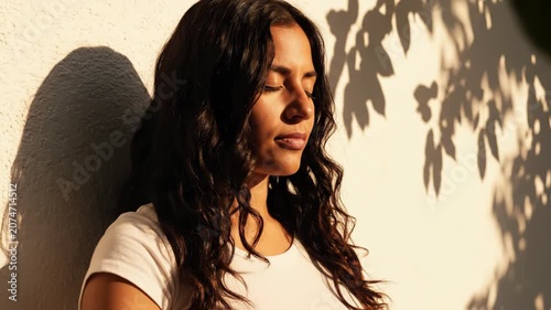 Serene woman meditating with prayer hands in sunlight.