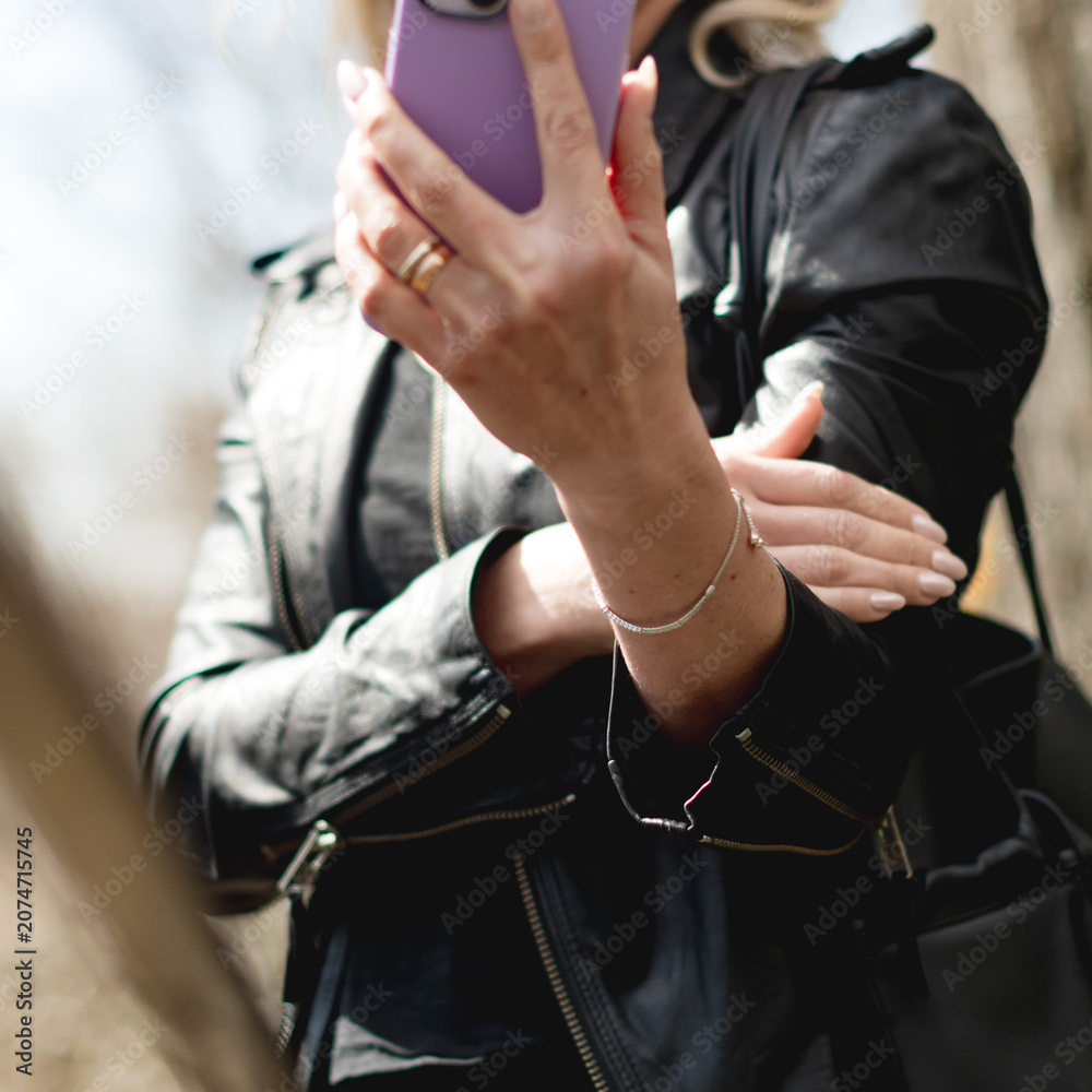 Fototapeta premium Busy modern woman with sunglasses and a black leather jacker on her mobile device outside on a cool fall afternoon.