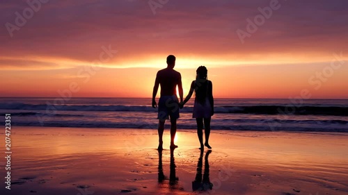 Romantic couple holding hands watching sunset on a beach