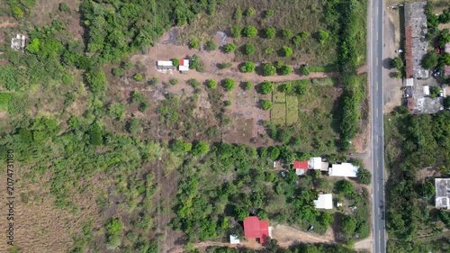 Aerial drone top-down view showing a remote ranch property with sparse structures, lush green trees, and dry grass fields on the coast of Guerrero, Mexico
