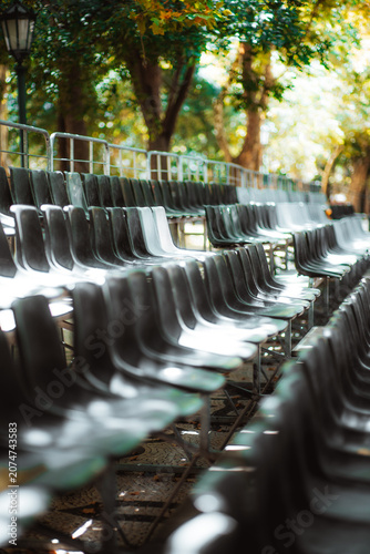Tableau sur toile Rows of empty plastic chairs in an outdoor venue under leafy trees, photographed