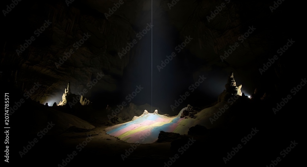 Naklejka premium Stunning shaft of natural light illuminating colorful prismatic reflections on the floor of a deep dark limestone subterranean cavern