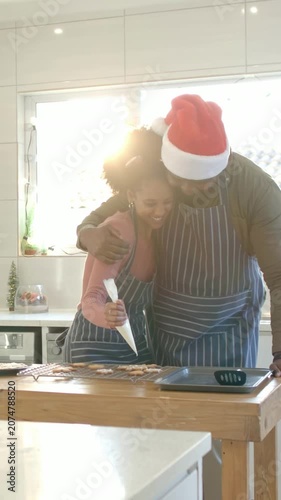 Vertical video: She piping holiday cookies with piping bag at island while man in Santa hat hugging