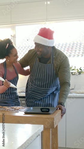 Vertical video: Talking, couple leaning and guiding, piping cookies with bag in kitchen, Santa hat