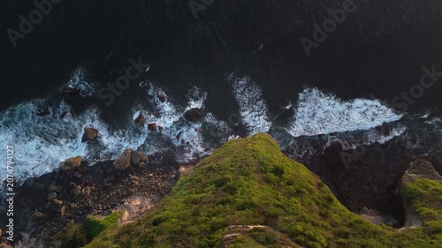 Cinematic drone footage of green volcanic cliffs meeting deep blue ocean during golden hour sunset in Bali. Perfect travel and adventure backdrop.