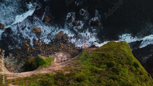 4K drone shot of Bali coastline with powerful sea surf washing over rocky formations at dusk. Premium tropical nature stock footage.