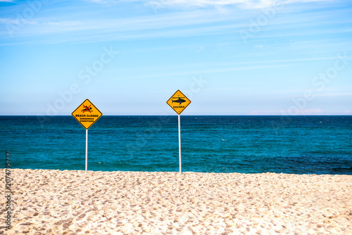 Shark warning and beach closure signs on Bronte Beach following a shark incident, with calm ocean and blue sky, Sydney, Australia.