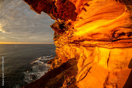 Foto Sunrise illuminates sculpted sandstone cliffs and coastal rock formations overlooking the Pacific Ocean along the Sydney coastline, New South Wales, Australia