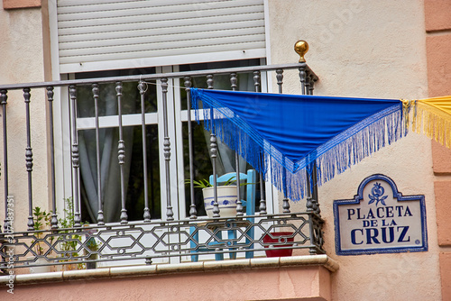 Foto Blue fringed shawl hanging from a residential balcony beside the Placeta de la Cruz street sign during Cruces de Mayo in Granada, Spain