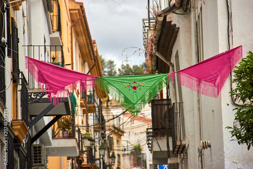 Foto Green embroidered shawl hanging between two pink fringed shawls above a narrow residential street during Cruces de Mayo in Granada, Spain