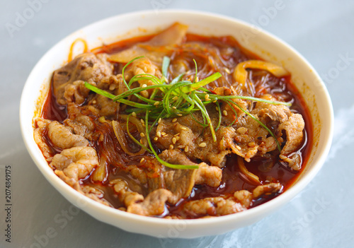 Bowl of hot mala spicy beef slices and clear glass noodles in rich red chili oil broth.
