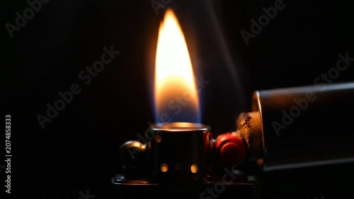 Close-up of a lit cigarette lighter with a bright flame and wisps of smoke.
