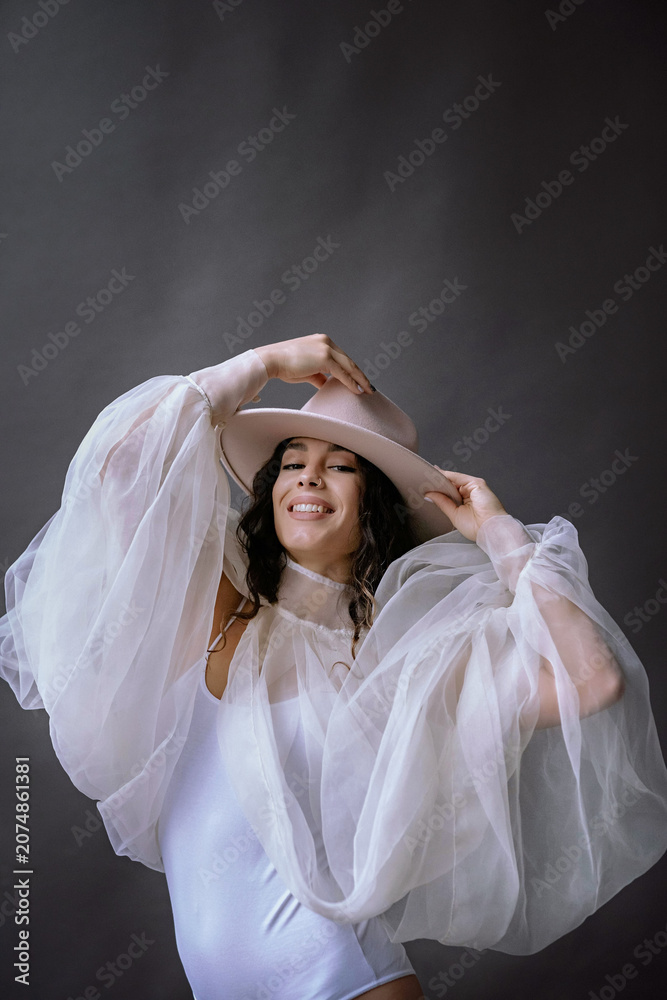Fototapeta premium Elegant woman in white outfit, posing with hat, dark backdrop