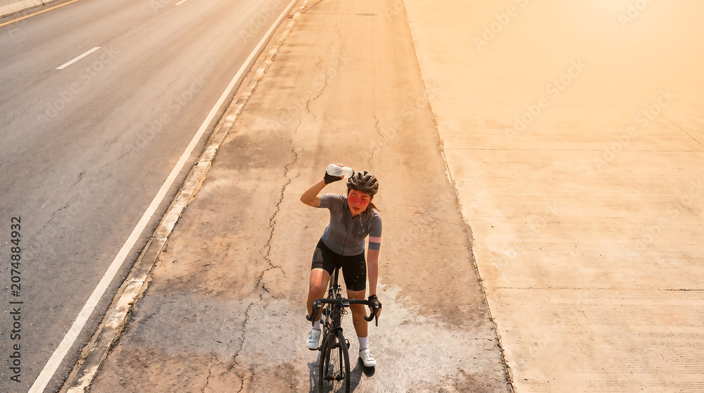 Obraz premium A cyclist battles a heat wave on a hot road, pouring water. Overhead view with clear copy space in the background, perfect for news and advertising.