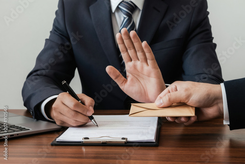 Man in suit refuses bribe money from colleague while signing document. Businessman rejects envelope with cash offer at office desk. Honest work ethic concept.