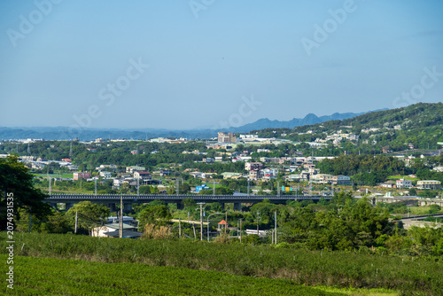 Fényképezés The verdant terraced fields of Tongluo Tea Plantation in Miaoli, the sea of ​​tung blossoms in the distant mountains, and the scenery of the Taiwan Railway train passing by